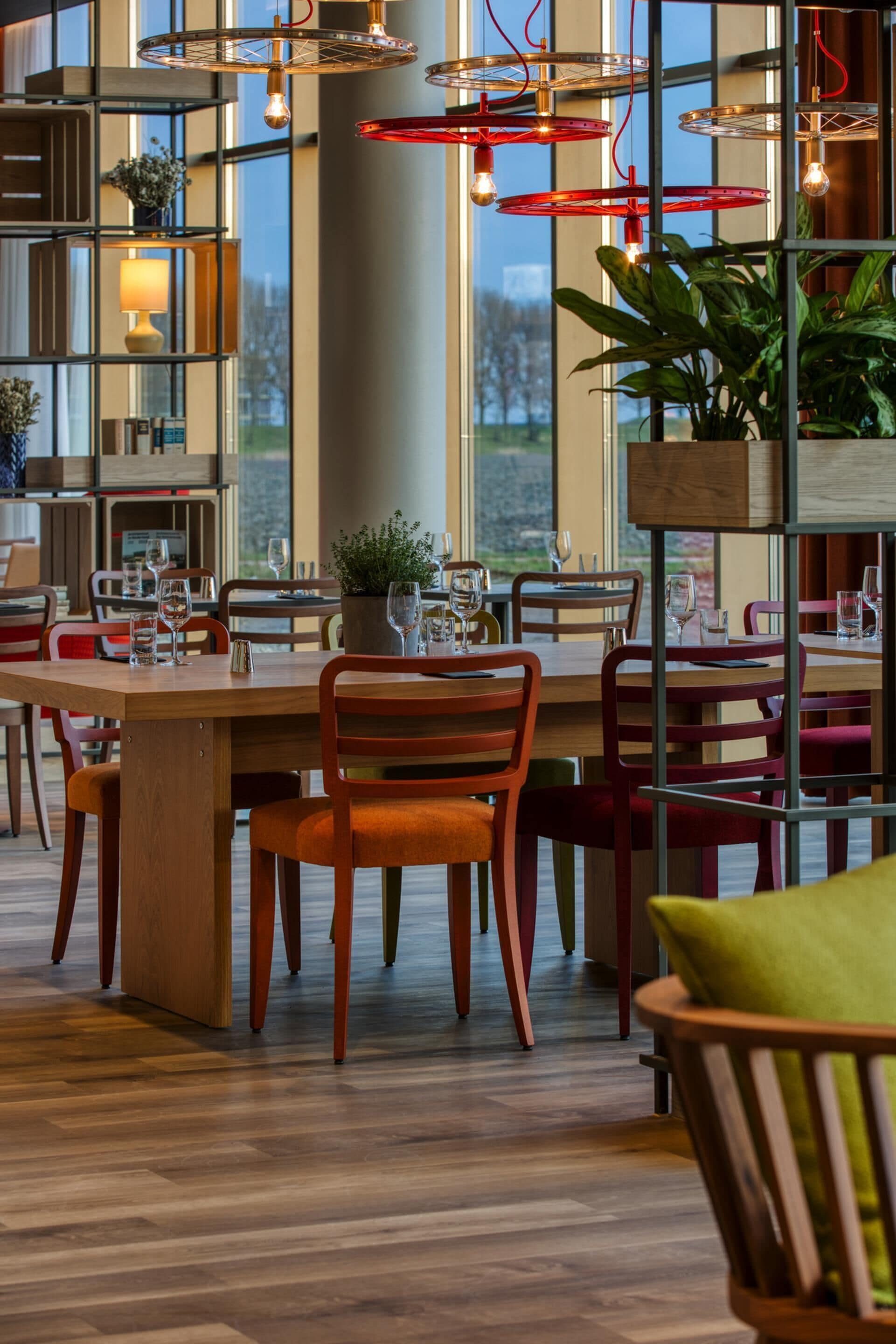 A modern dining area with wooden tables, red chairs, and hanging pendant lights.