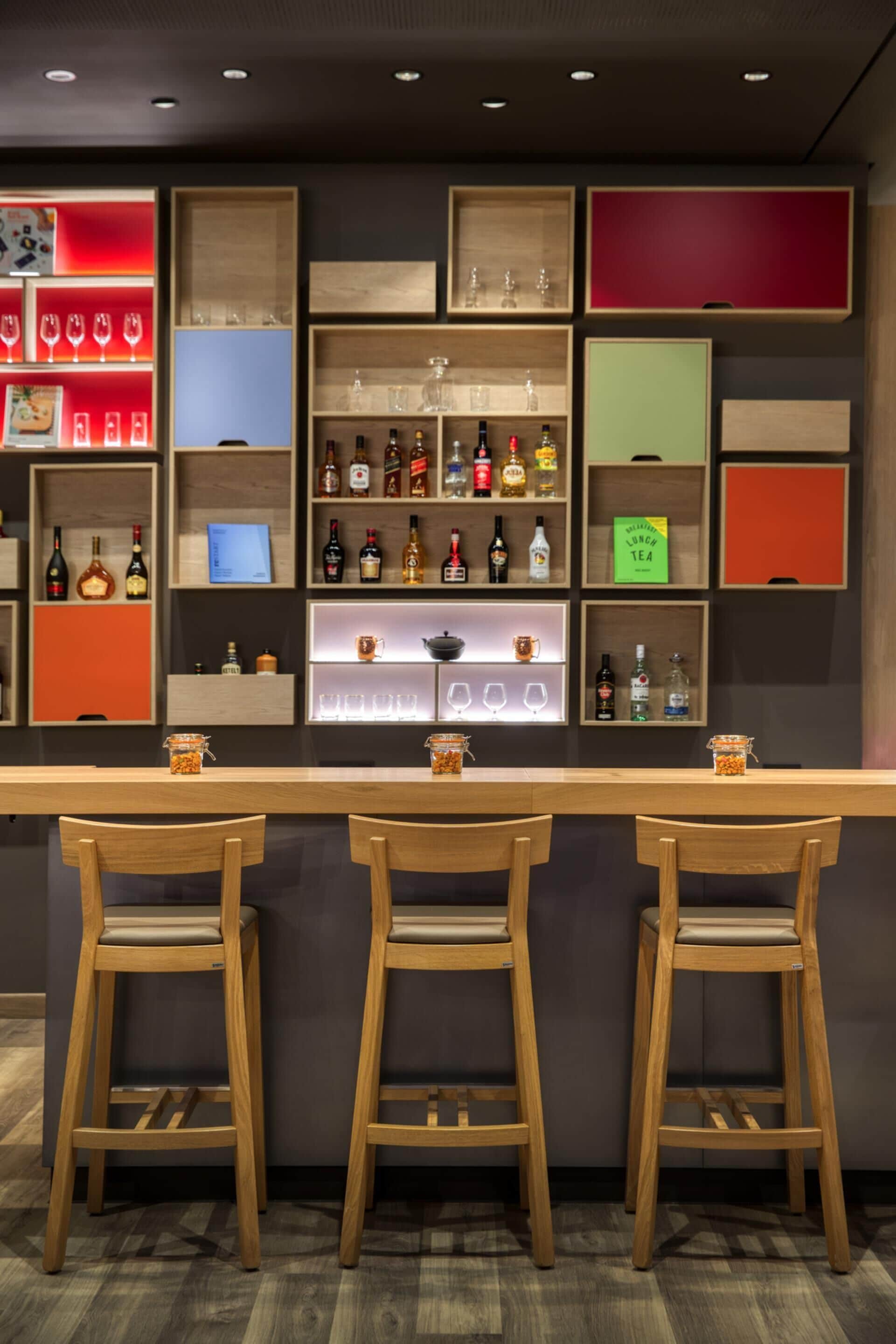 Zona de bar con taburetes de madera, estanterías con botellas, vasos y una pizarra con el menú.