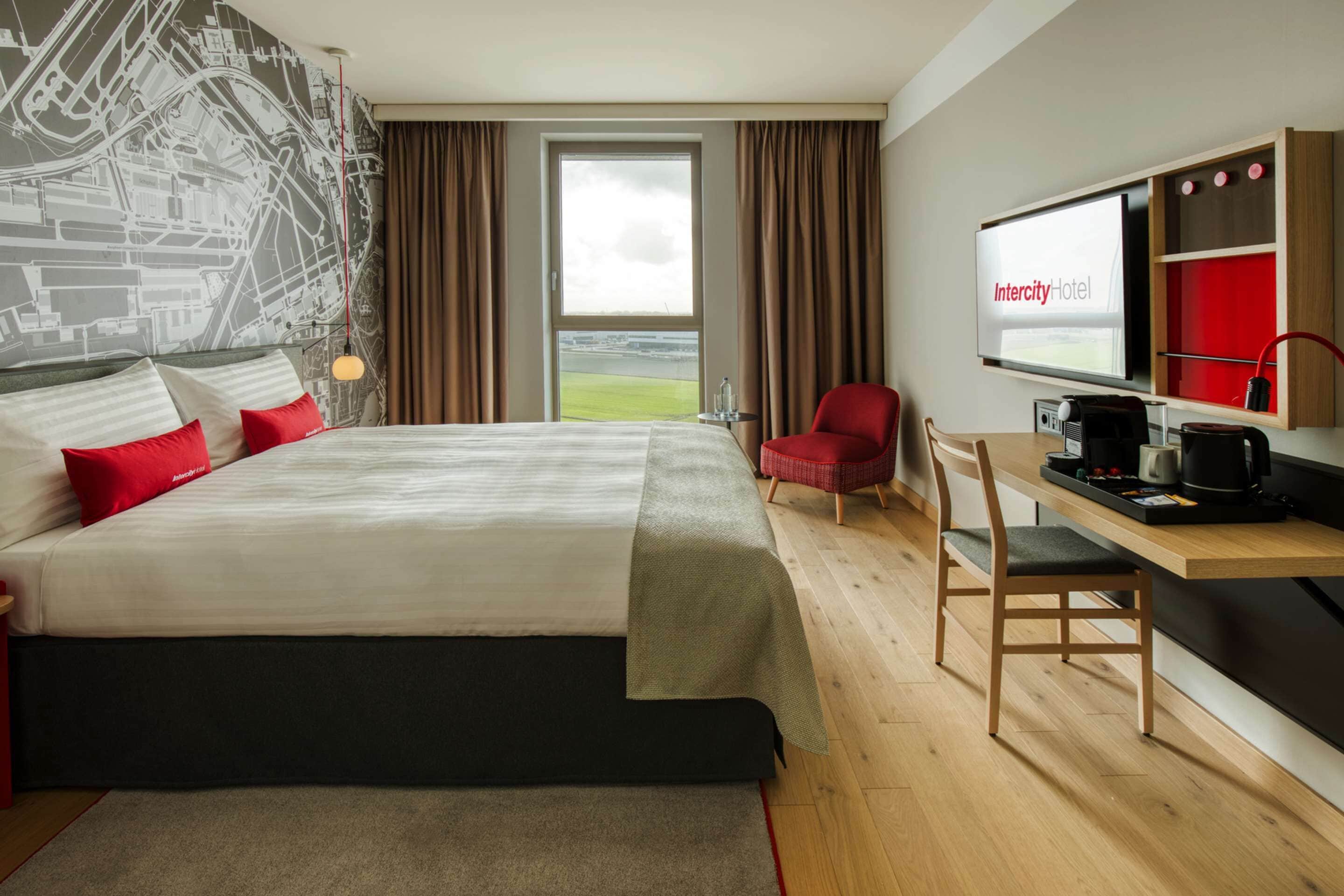Habitación de hotel con una cama grande, un escritorio con cafetera, un televisor y vistas a la ciudad.