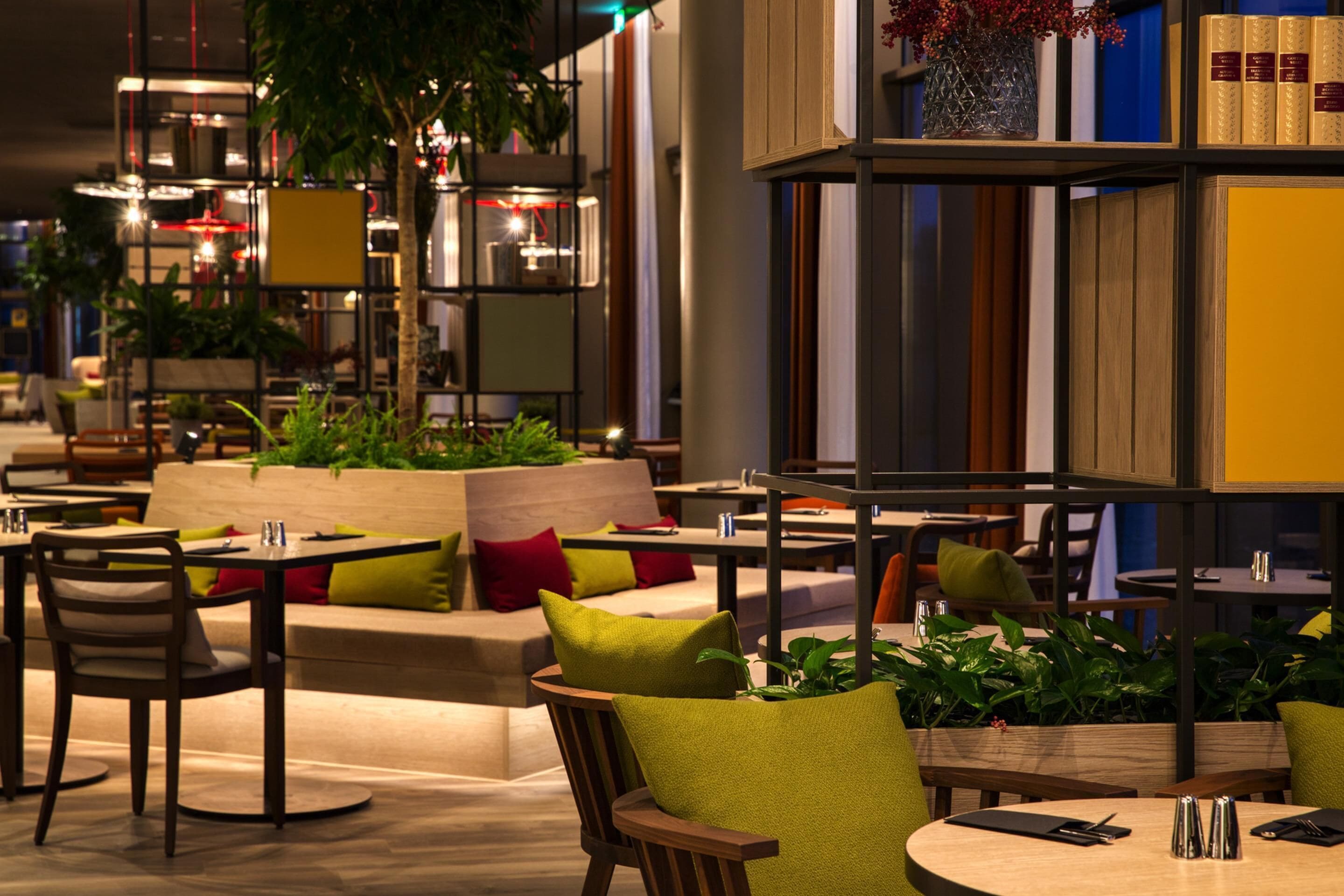 Een moderne zithoek met ronde tafels, comfortabele stoelen en verschillende planten.