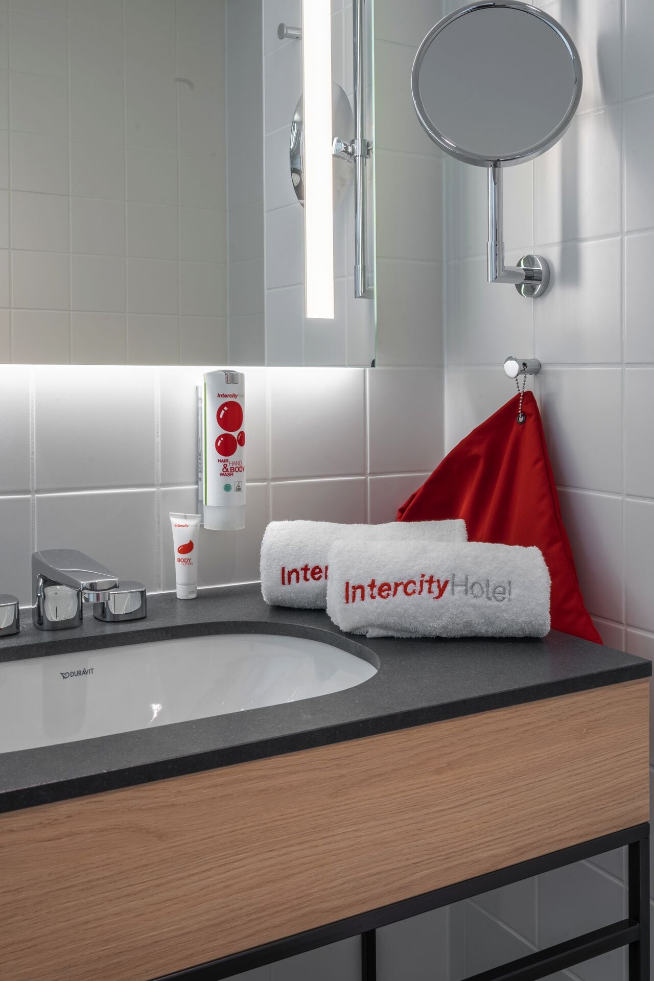 Een moderne badkamer met een groot wastafel, een spiegel en een handdoekrek met een rode handdoek.