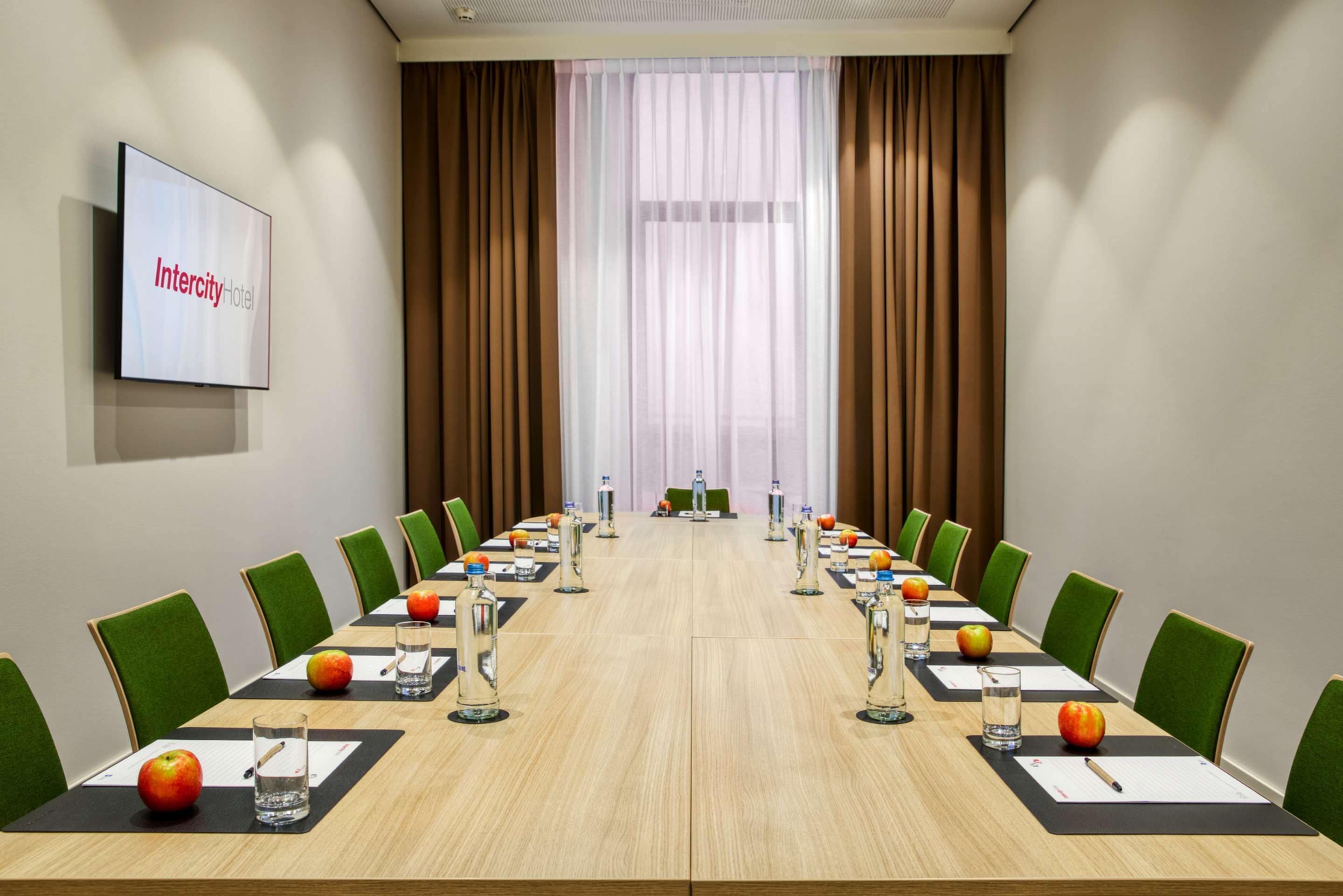 Een vergaderruimte met een lange tafel, groene stoelen en een appel op elke zitplaats.