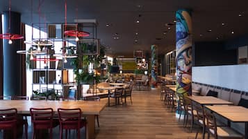 A modern restaurant with wooden tables and chairs, red hanging lights, and a colorful mural on the wall.