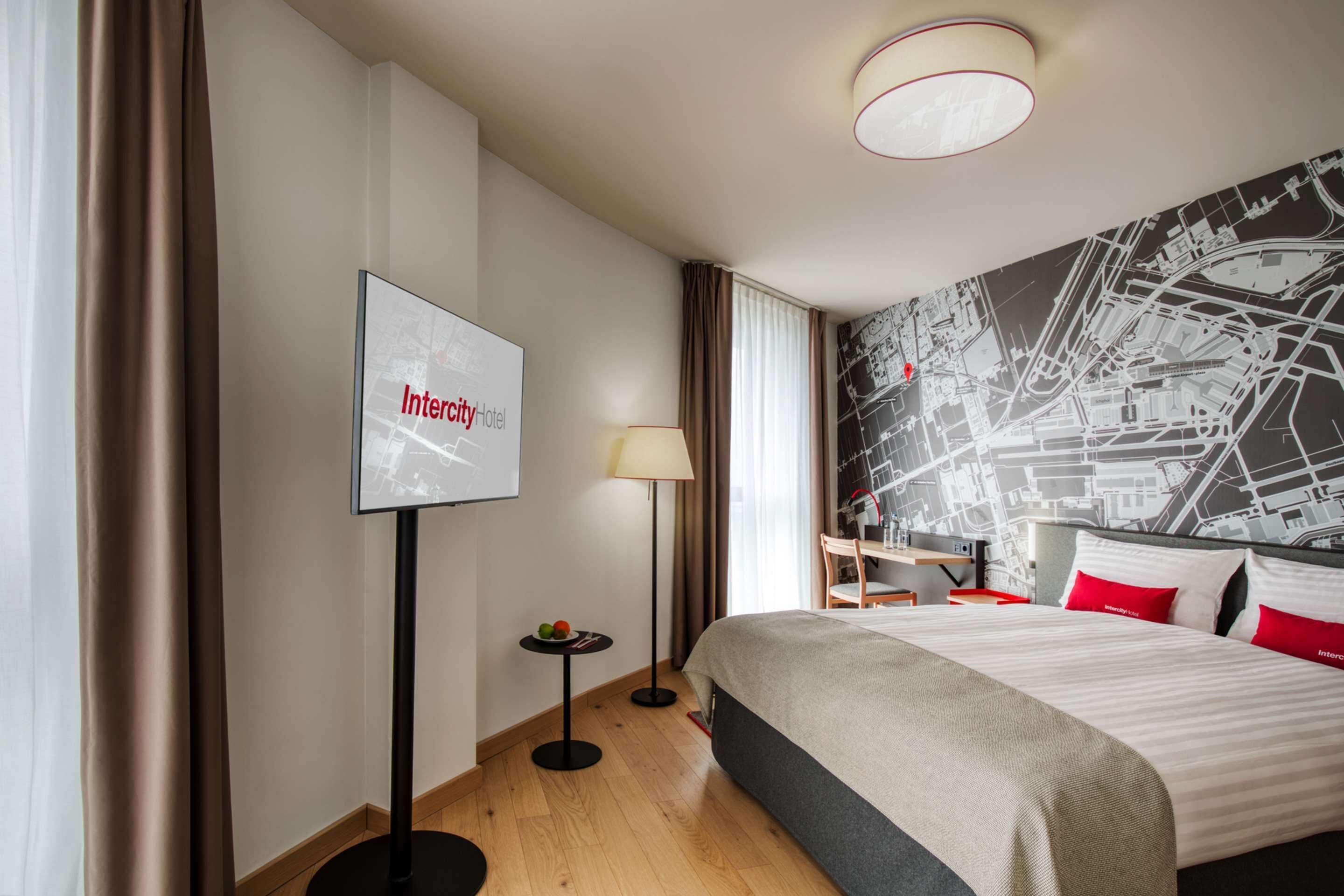 Habitación de hotel con cama, un mural de mapa, televisor, lámpara y una pequeña mesa con frutas.