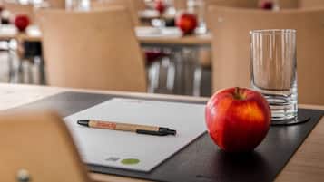 Una mesa de comedor con una pluma, una manzana y un vaso de agua sobre un mantel individual.