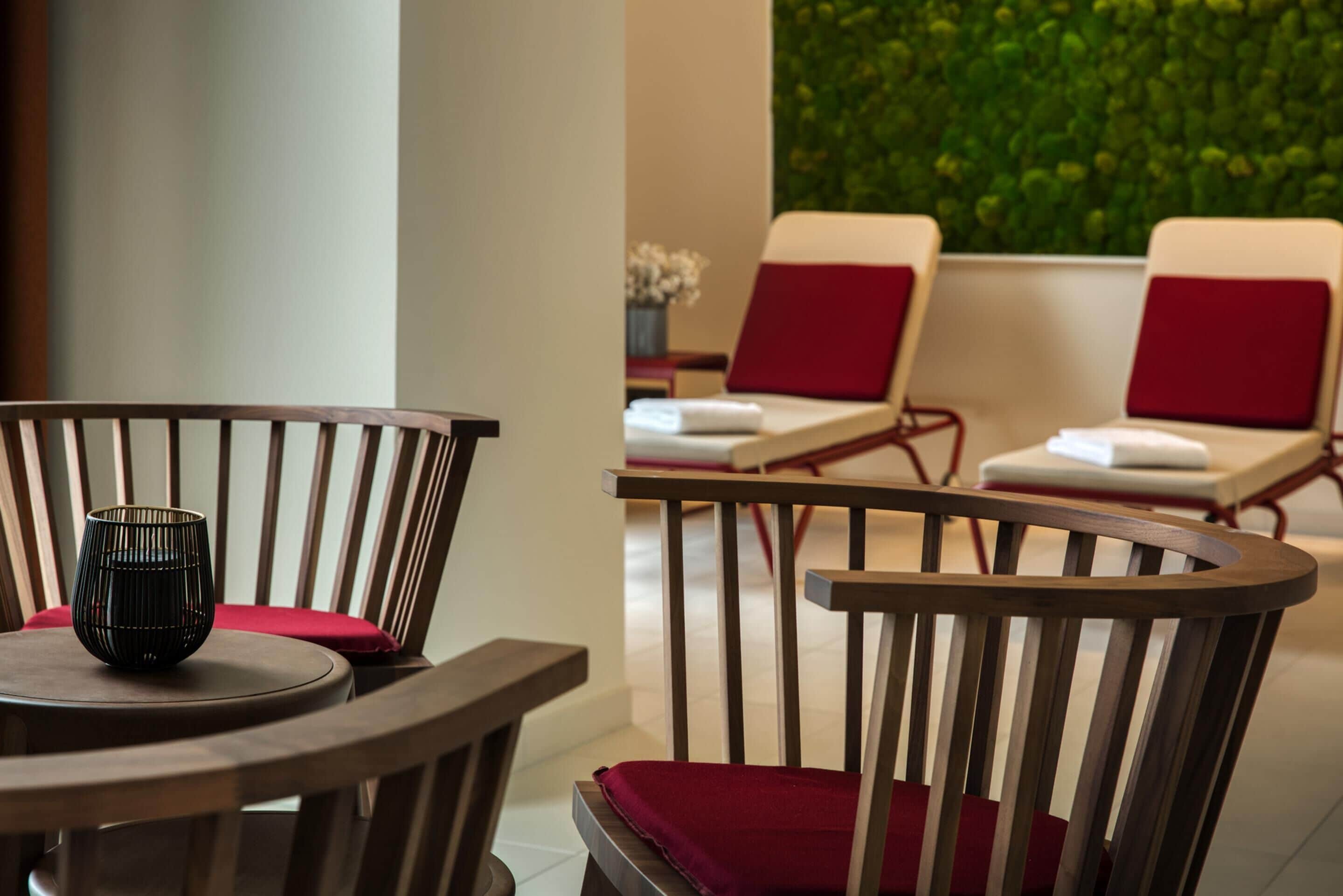 A wooden chair with a red cushion, a small table, and a wall with a green plant.