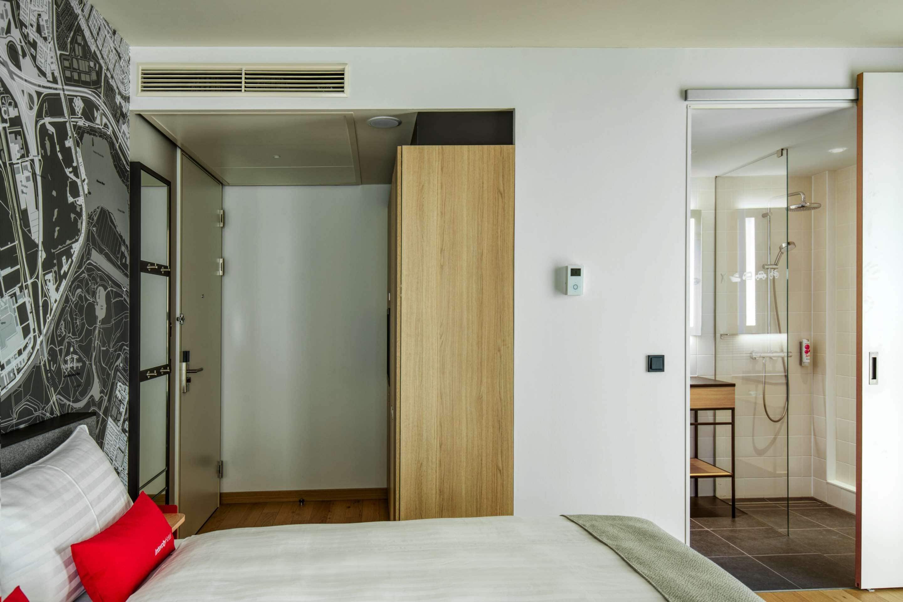 Une chambre d’hôtel moderne équipée d’un lit, d’une armoire en bois, d’une salle de bain avec douche et d’une carte géographique murale.