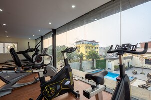 Un gimnasio con bicicletas estáticas y una caminadora, ventanas amplias con vistas a una zona residencial.