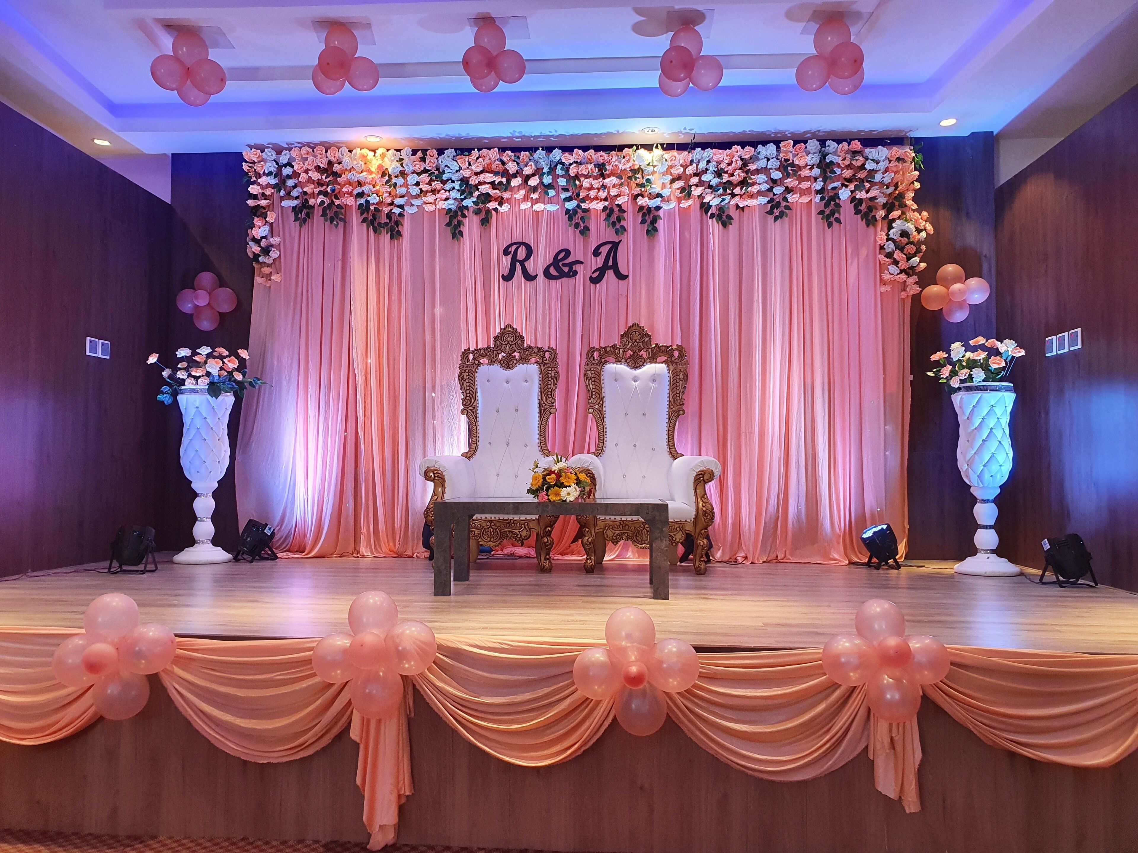 Un escenario con una silla ornamentada en blanco y dorado, cortinas rosadas y decoraciones florales.