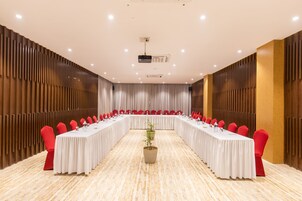Un salón de conferencias con una larga mesa, sillas rojas y un proyector.