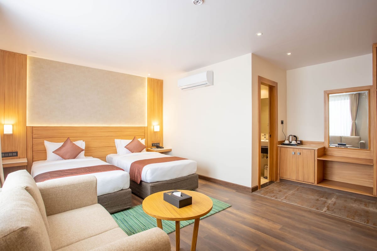 A hotel room with two beds, a sofa, a small table, a mirror, and a kitchenette.