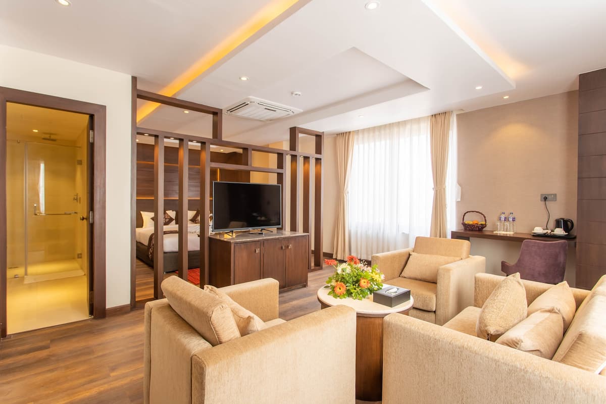 A modern hotel room with a living area, a TV, a sofa set, a coffee table, and a small kitchen area.