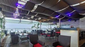 Un espacio al aire libre con mobiliario de mimbre y cojines rojos, una zona de bar y vistas al mar.