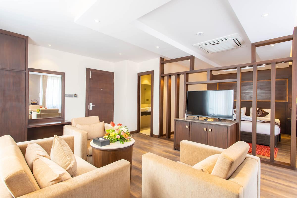 A modern hotel room with a sofa, a TV, and a wooden cabinet.
