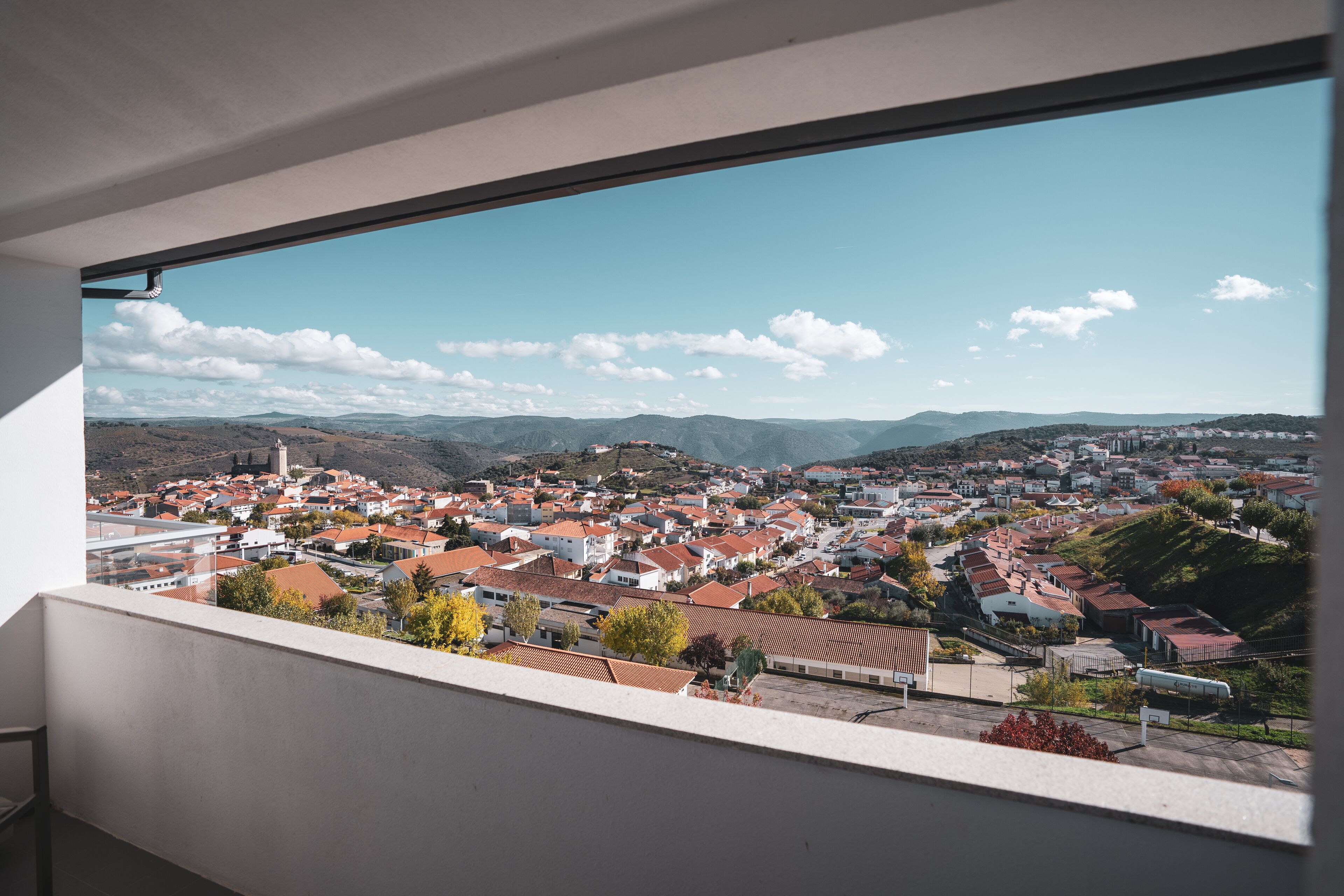 Una vista panorámica de un pueblo con edificios de techo rojo, cielo despejado y montañas distantes.