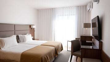 A hotel room with two beds, a desk with a chair, a television, and an air conditioning unit.