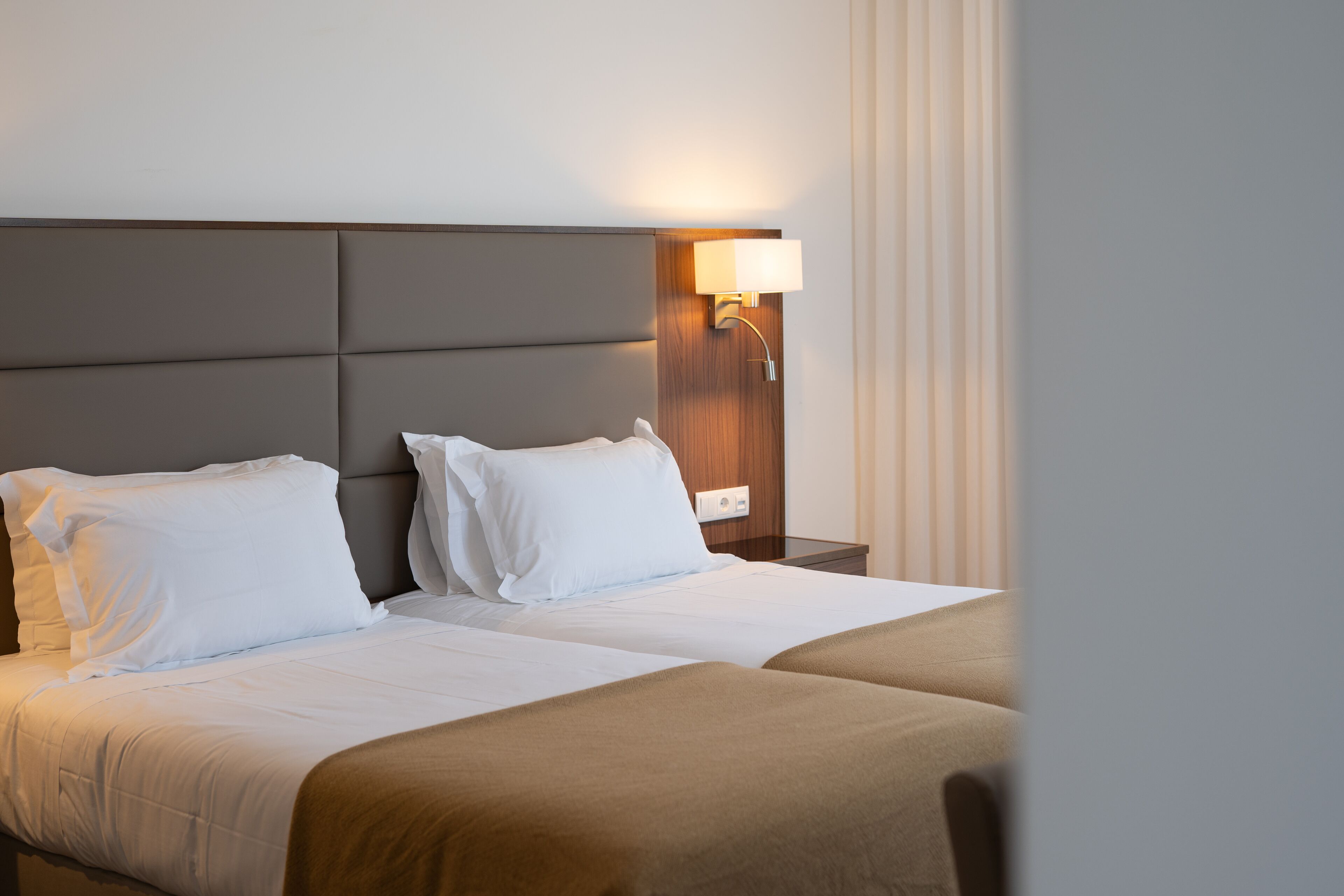 A hotel room with a large bed, two pillows, a nightstand with a lamp, and a wooden headboard.