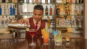 Un barman preparando una bebida en la barra, con estantes llenos de botellas de licor al fondo.