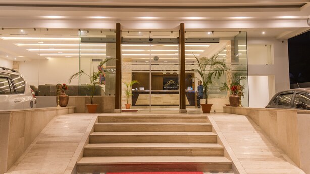Un hall de hotel con una recepción, una escalera que sube al piso superior y plantas en macetas.