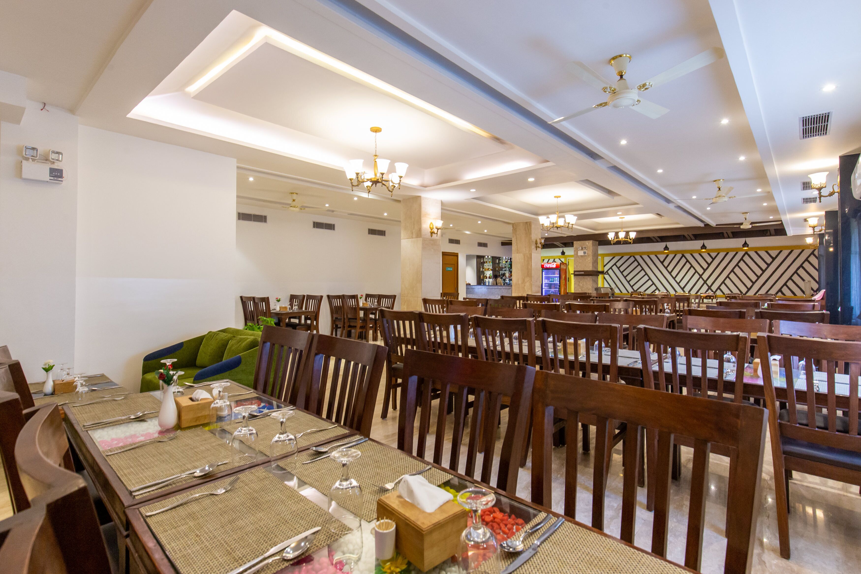 Une salle à manger spacieuse, dotée de plusieurs tables, de chaises en bois et de ventilateurs de plafond.