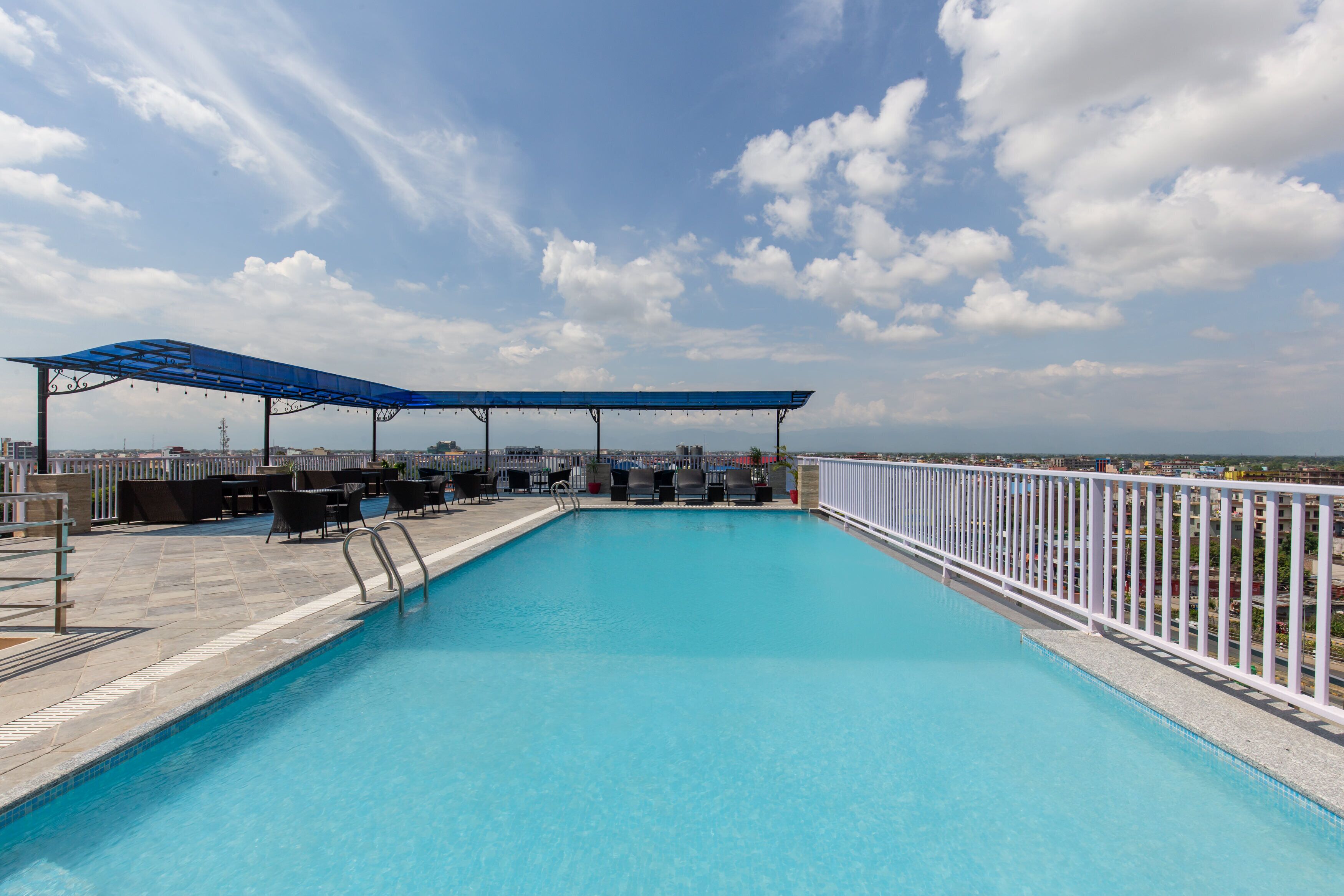 A rooftop swimming pool with a blue canopy, outdoor seating, and a city view.