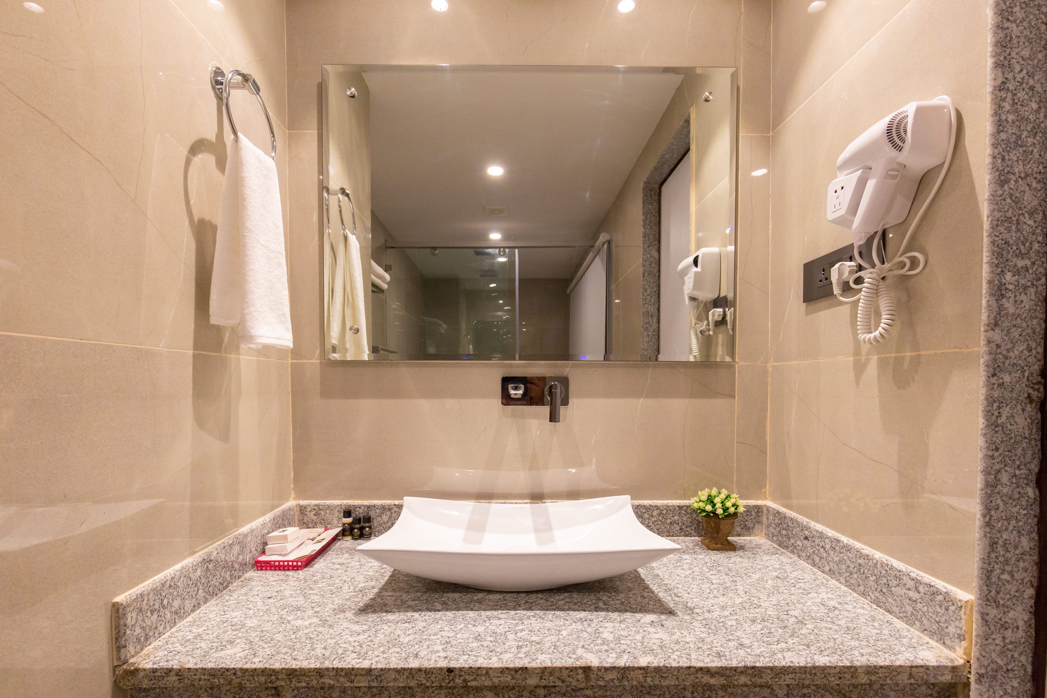 Un baño con un espejo grande, un lavabo con recipiente, un secador de pelo y un perchero para toallas.