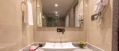 Un baño con un espejo grande, un lavabo con recipiente, un secador de pelo y un perchero para toallas.