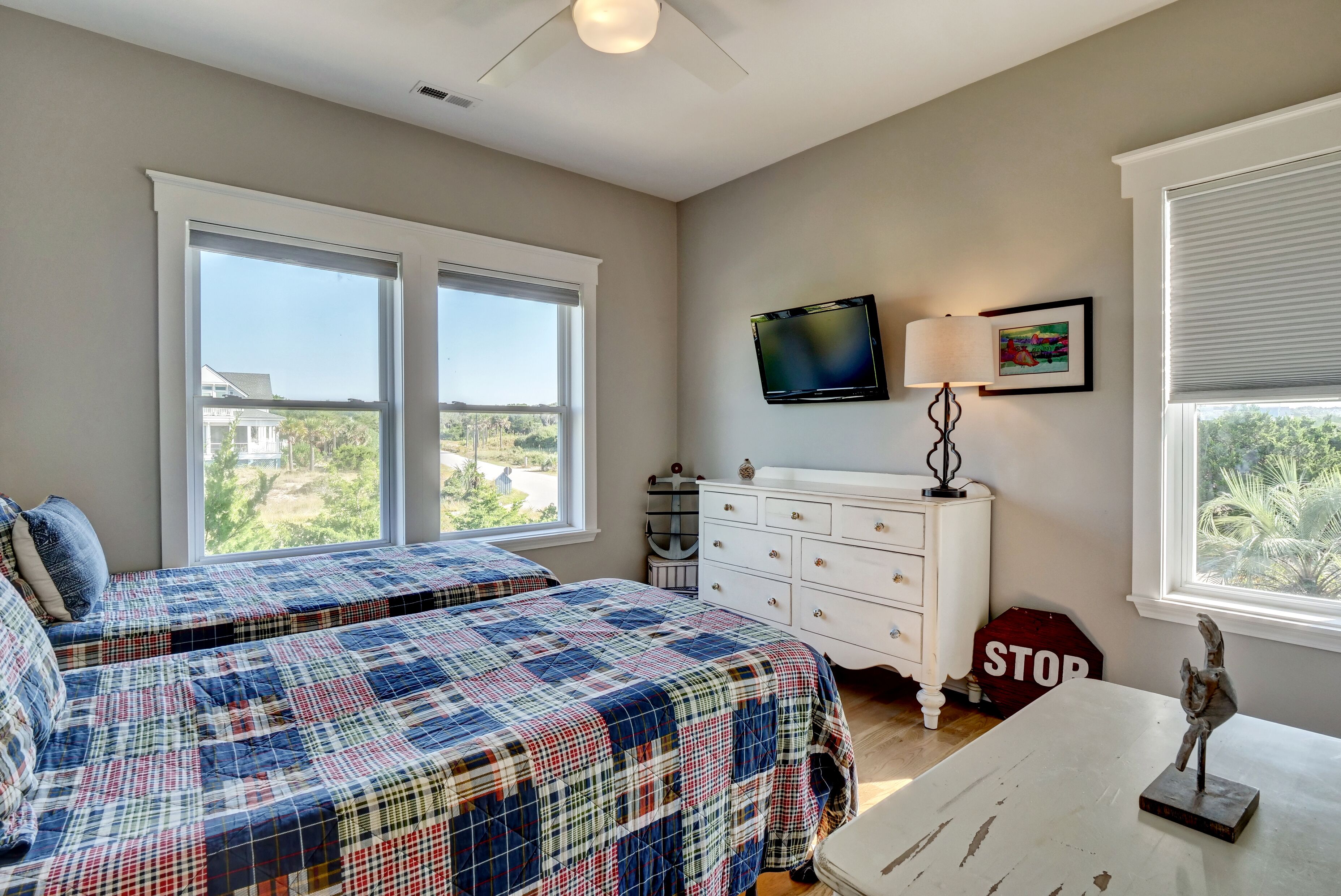 A bedroom with two beds, a dresser, a television, and a window with a view of the outdoors.