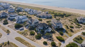 A coastal residential area with houses featuring large windows and balconies, surrounded by a sandy beach and ocean. - Bald Head Island. Oceanfront 2nd Row. 4 bedrooms. 3.5 baths. BHI Club access. (Bald Head Island)