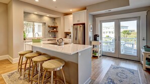 A modern kitchen with a central island, bar stools, and a view of the outside. - Bald Head Island. Oceanfront 2nd Row. 4 bedrooms. 3.5 baths. BHI Club access. (Bald Head Island)