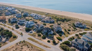 An aerial view of a coastal residential area with houses, roads, and a beach. - Bald Head Island. Oceanfront 2nd Row. 4 bedrooms. 3.5 baths. BHI Club access. (Bald Head Island)