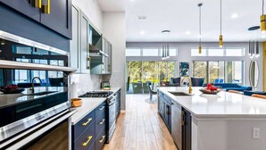 A modern kitchen with a central island, built-in appliances, and a view to an outdoor seating area. - Rare Home w Golf Simulator, Sci-Fi Theme BR, Arcade, Theater & Gym - Near Parks (Davenport)
