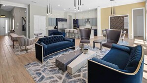 A modern living room with a dark blue sofa set, a coffee table, and a dining area with a high table and chairs. - Rare Home w Golf Simulator, Sci-Fi Theme BR, Arcade, Theater & Gym - Near Parks (Davenport)