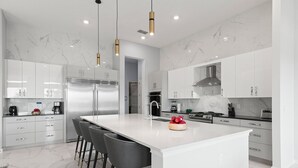 Een moderne keuken met een groot eiland, roestvrijstalen apparatuur en marmeren vloeren.