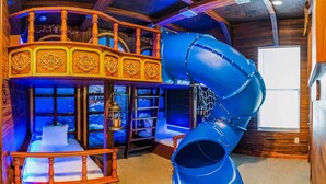 Zona de juegos con un tobogán, una casita de madera y una ventana con vistas al mar.