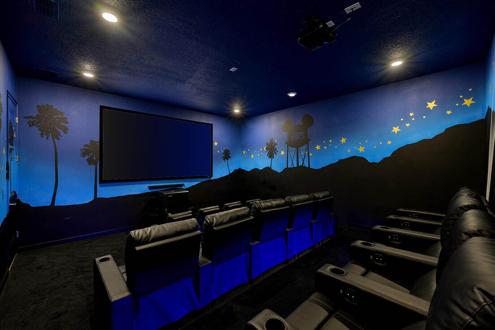 A home theater room with a large screen, reclining seats, and a starry wall mural.