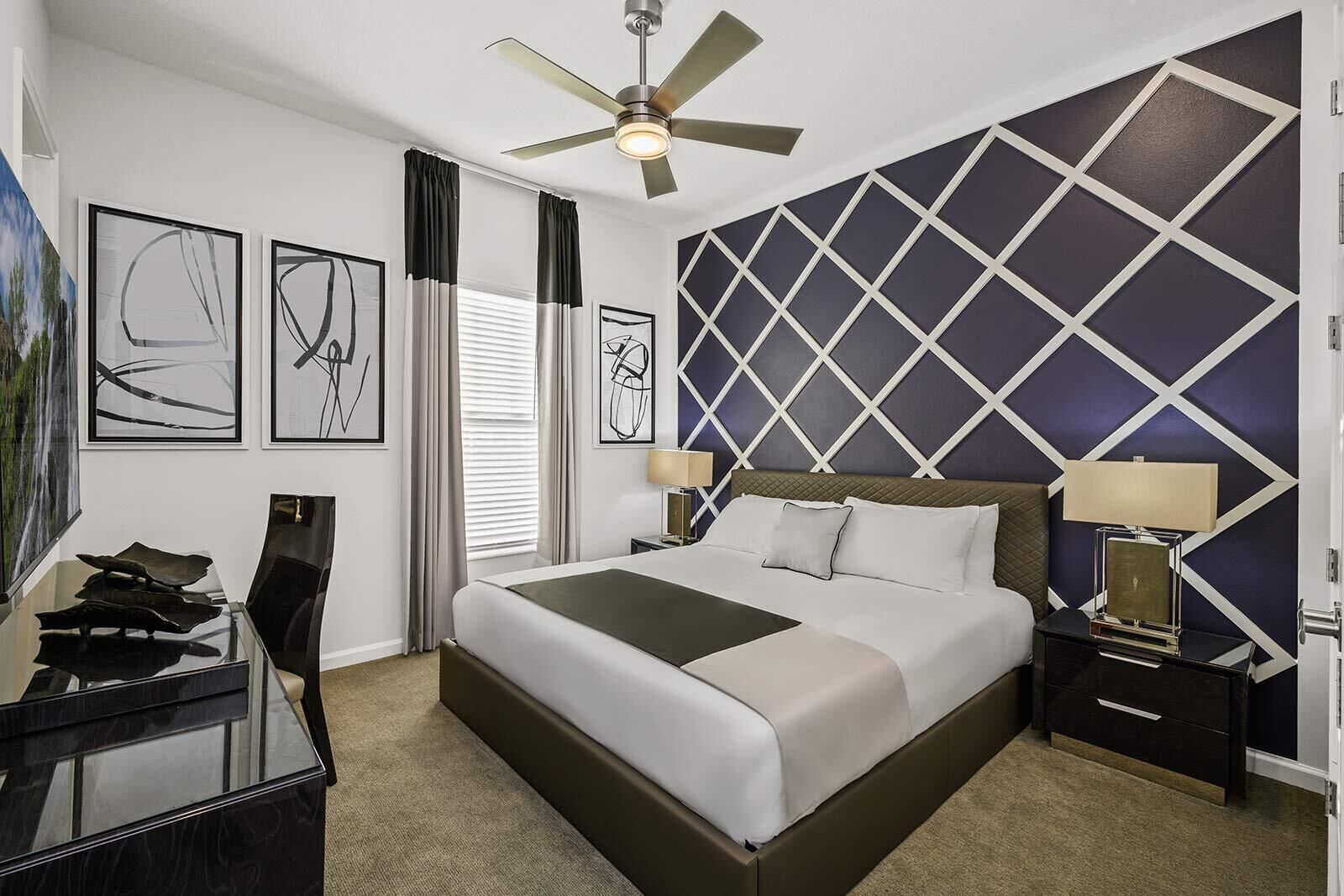 A modern hotel room with a large bed, a ceiling fan, and artwork on the walls.