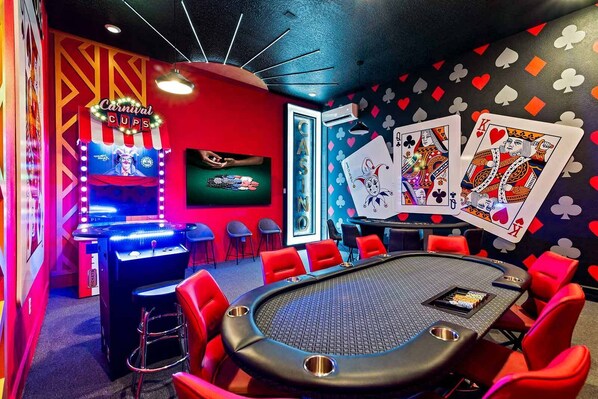Una sala de casino con una mesa de blackjack, sillas rojas y una pared decorada con cartas de juego.