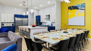 A modern kitchen with blue cabinets, a central island, and a dining area with a glass table and black chairs.