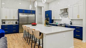 A modern kitchen with white marble backsplash, blue cabinets, stainless steel appliances, and a central island with bar stools.
