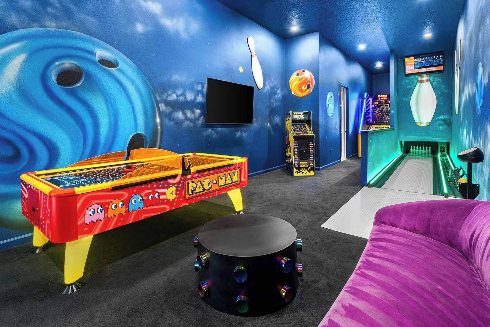 A room with a Pac-Man arcade machine, a bowling alley, and a large screen.