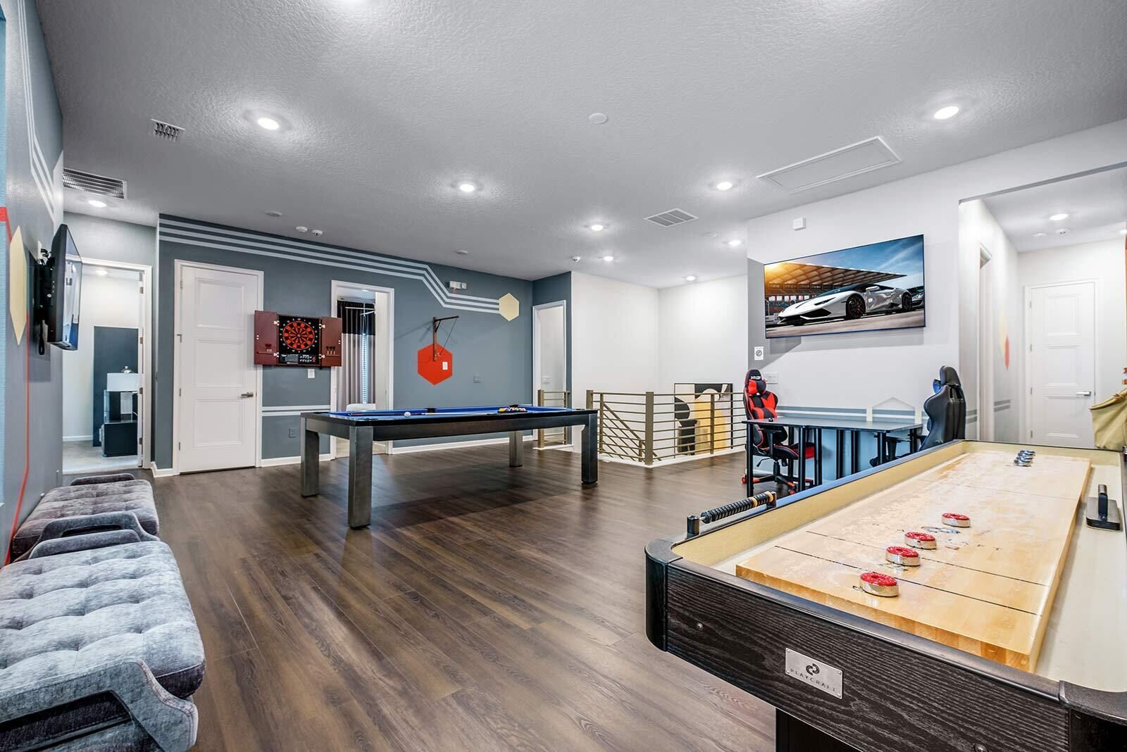 Un área recreativa moderna en interior con mesa de billar, mesa de futbolín y dardos.