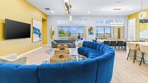 A modern living room with a blue sectional sofa, a flat-screen TV, and a dining area with a table and chairs. - Elegant Home w/ Ice Themed BR, Bowling, Karaoke RM, Theater & Gym - Near Parks (Davenport)