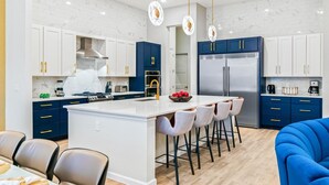 A modern kitchen with white and blue cabinetry, a central island with bar stools, and stainless steel appliances. - Elegant Home w/ Ice Themed BR, Bowling, Karaoke RM, Theater & Gym - Near Parks (Davenport)