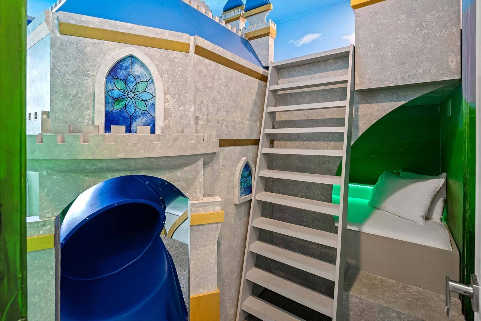 Zona de juegos infantiles con un tobogán, una escalera y una cama con iluminación verde.