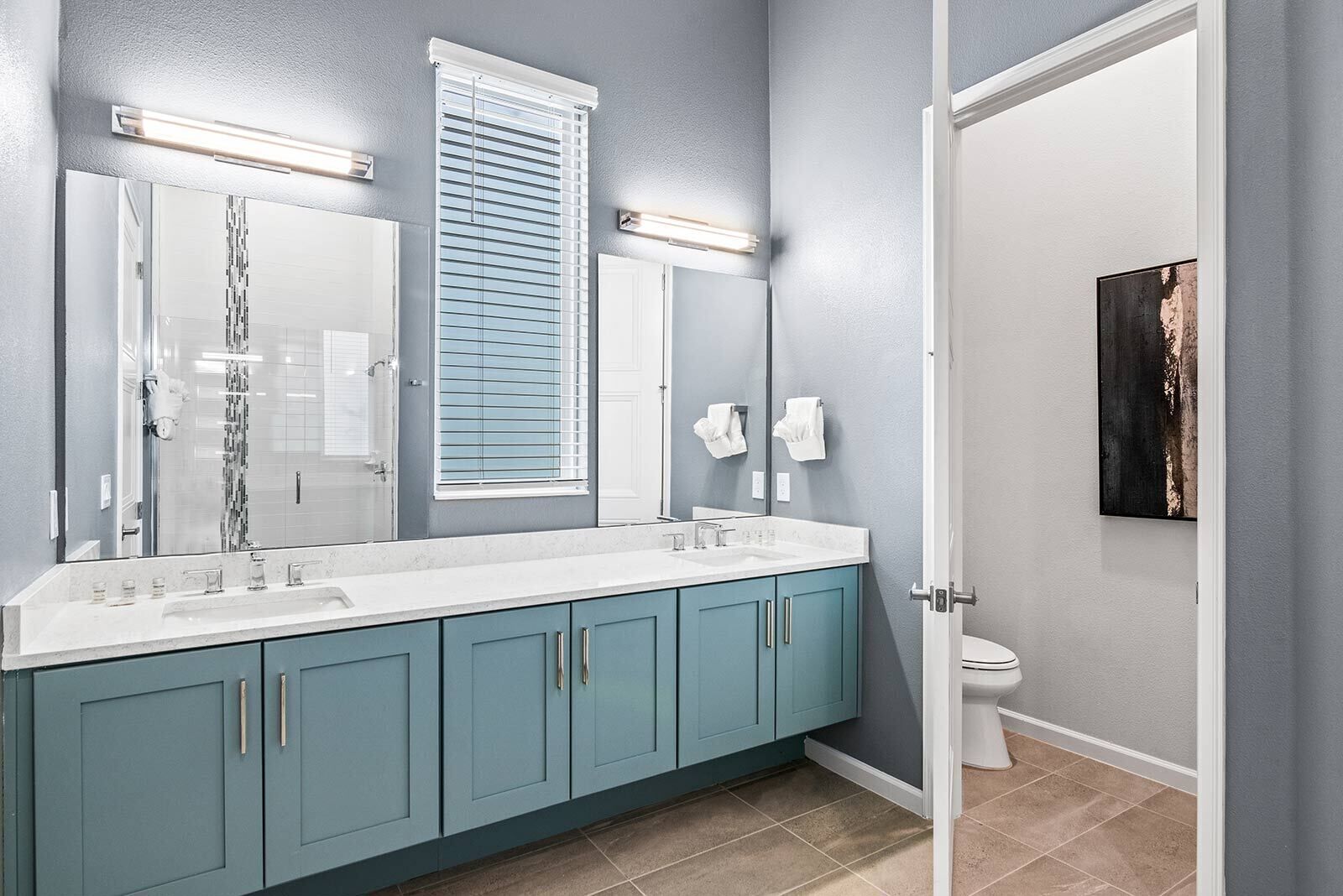 Un bagno con doppio lavandino, uno specchio grande e una finestra con persiane.