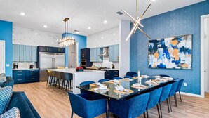 A modern kitchen with blue cabinets, a central island, and a dining area with blue chairs. - Homes by Villatel | Music Studio, Bowling, Pirate BR, Theater & Gym, Near Disney (Davenport)