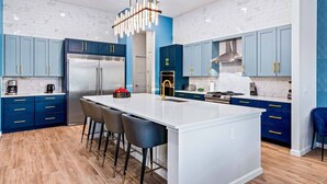 A modern kitchen with a central island, blue cabinets, stainless steel appliances, and a marble backsplash. - Homes by Villatel | Music Studio, Bowling, Pirate BR, Theater & Gym, Near Disney (Davenport)