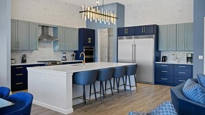 A modern kitchen with a central island, bar stools, and a stainless steel refrigerator.