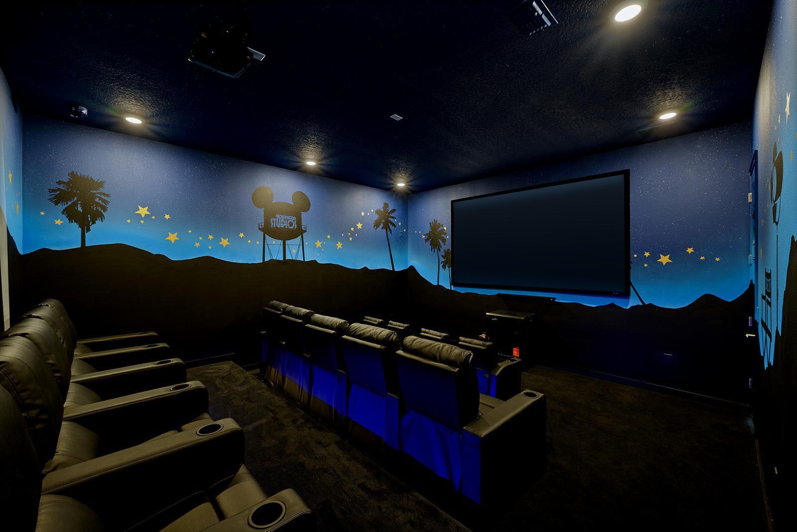 A home theater room with a large screen, reclining seats, and a starry wall mural.